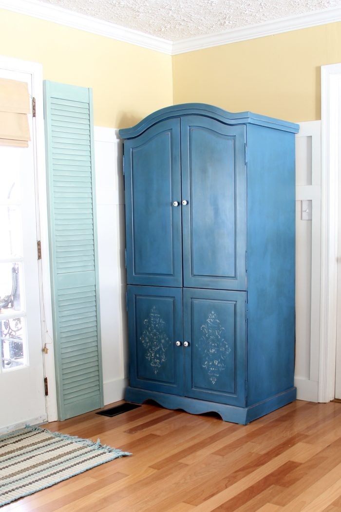 dark blue armoire with yellow walls and green shutters beside it