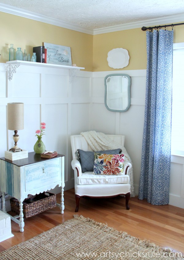 white walls with white chair and colorful pillow and french cabinet beside chair