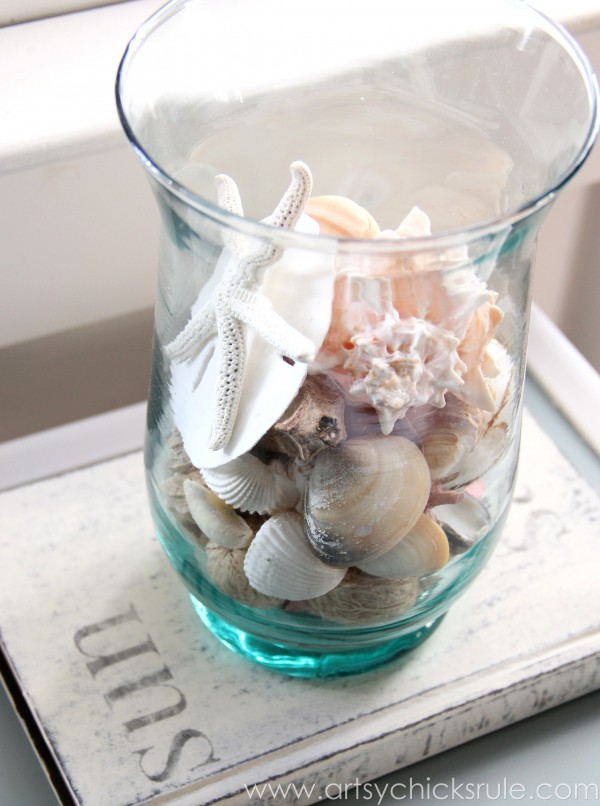 glass jar of seashells on white painted book