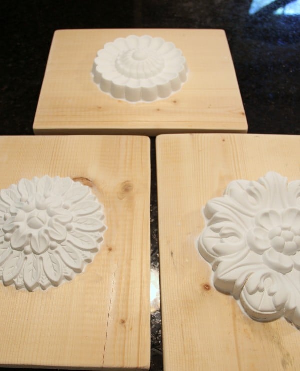 Three wooden boards each display a different ornate wood medallion featuring intricate white plaster floral and geometric designs, arranged on a dark surface.