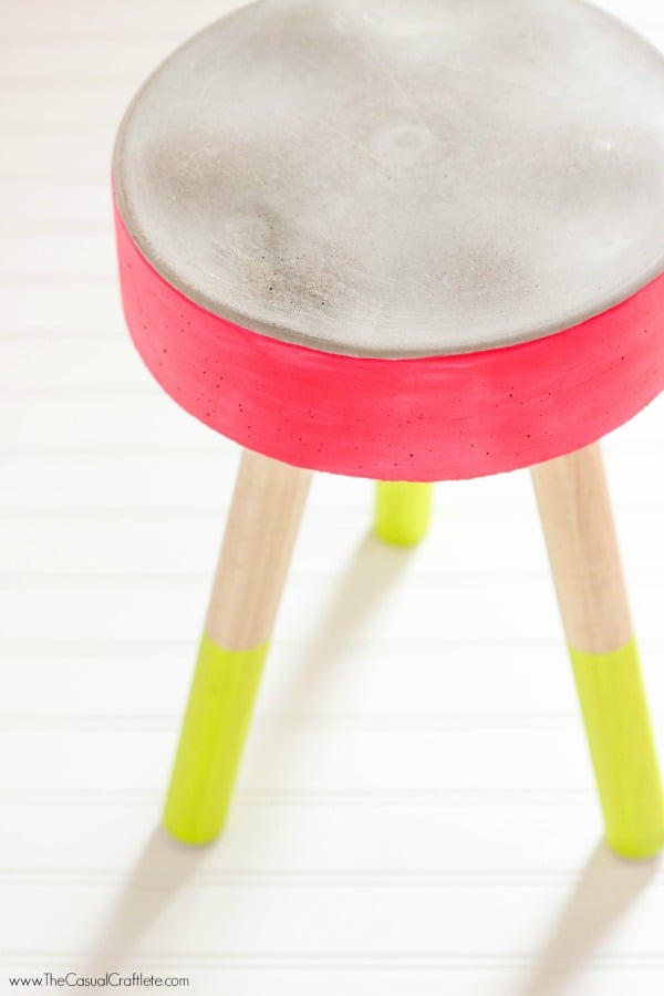 A concrete stool painted pink with yellow legs.