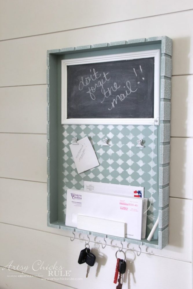 aqua tray with area that is chalkboard at top, clips for notes, and mail area with hangers on bottom for keys hanging on wall