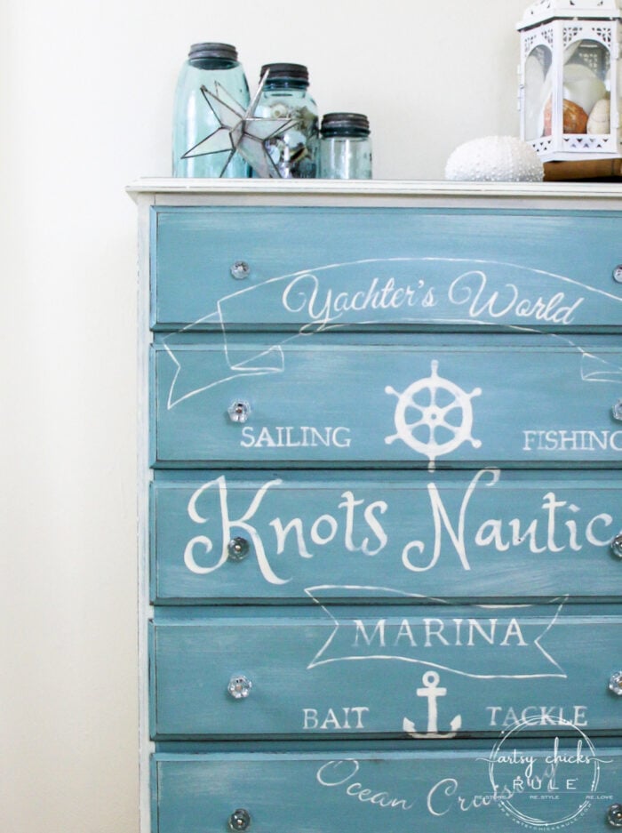 A blue dresser with white nautical-themed words and symbols, such as an anchor and ship wheel. Chalk paint highlights the coastal décor style, though it's important to know the pros and cons of chalk paint before starting similar projects.