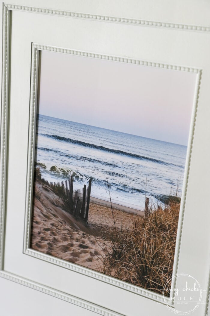 This beach scene wall art cost me SIX dollars! Yep! An old thrift store find, white spray paint and my own photo....budget friendly wall art! artsychicksrule.com #wallart #beachscenewallart #coastalwallart #diywallart #diybeachscene #framedbeachart