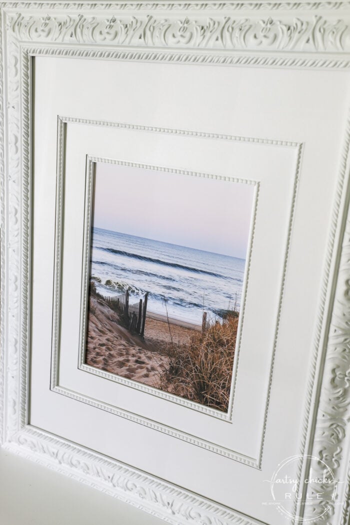 This beach scene wall art cost me SIX dollars! Yep! An old thrift store find, white spray paint and my own photo....budget friendly wall art! artsychicksrule.com #wallart #beachscenewallart #coastalwallart #diywallart #diybeachscene #framedbeachart