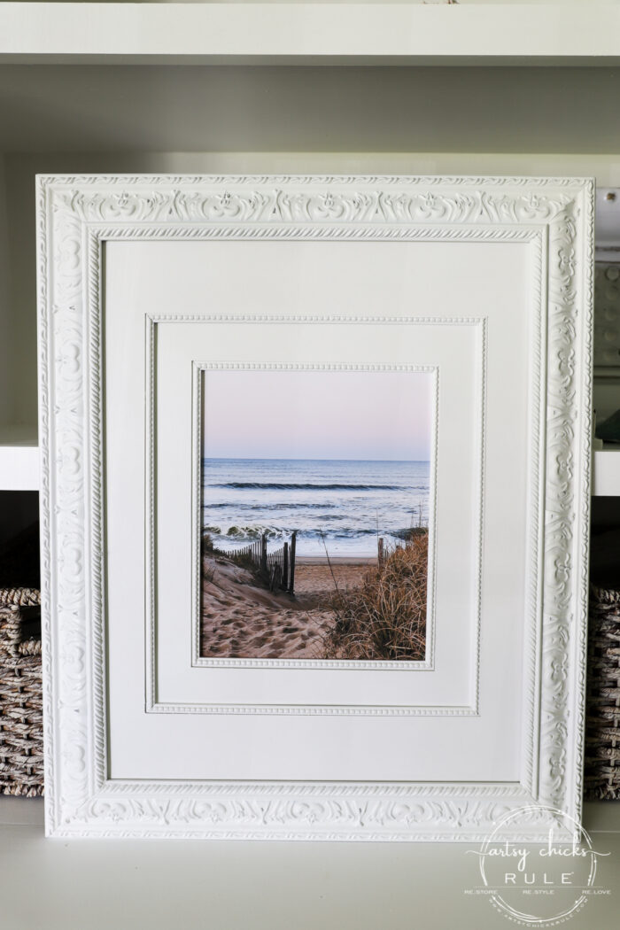 This beach scene wall art cost me SIX dollars! Yep! An old thrift store find, white spray paint and my own photo....budget friendly wall art! artsychicksrule.com #wallart #beachscenewallart #coastalwallart #diywallart #diybeachscene #framedbeachart