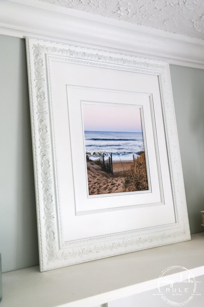 This beach scene wall art cost me SIX dollars! Yep! An old thrift store find, white spray paint and my own photo....budget friendly wall art! artsychicksrule.com #wallart #beachscenewallart #coastalwallart #diywallart #diybeachscene #framedbeachart