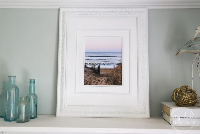 This beach scene wall art cost me SIX dollars! Yep! An old thrift store find, white spray paint and my own photo....budget friendly wall art! artsychicksrule.com #wallart #beachscenewallart #coastalwallart #diywallart #diybeachscene #framedbeachart