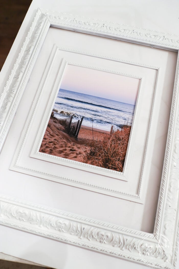 This beach scene wall art cost me SIX dollars! Yep! An old thrift store find, white spray paint and my own photo....budget friendly wall art! artsychicksrule.com #wallart #beachscenewallart #coastalwallart #diywallart #diybeachscene #framedbeachart