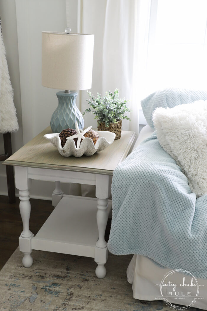 bleached wood table top with white base beside couch with blue blanket