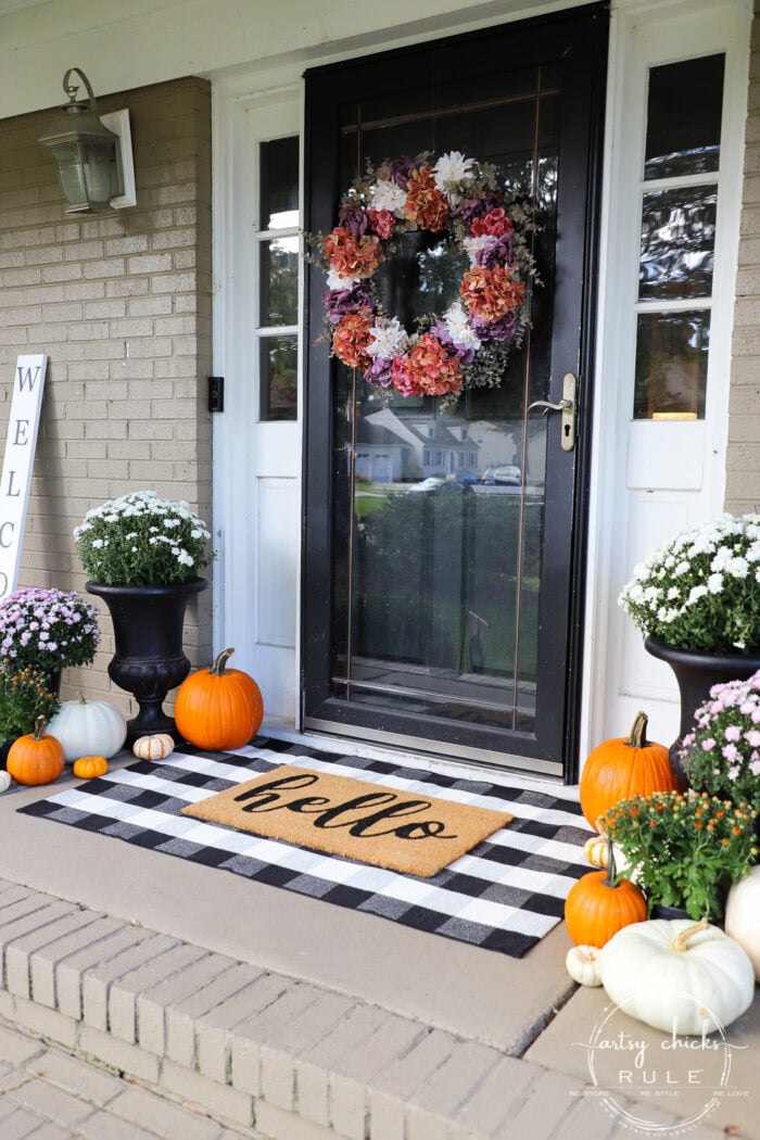front door on porch with pumpkins, mums and fall decor surrounding it