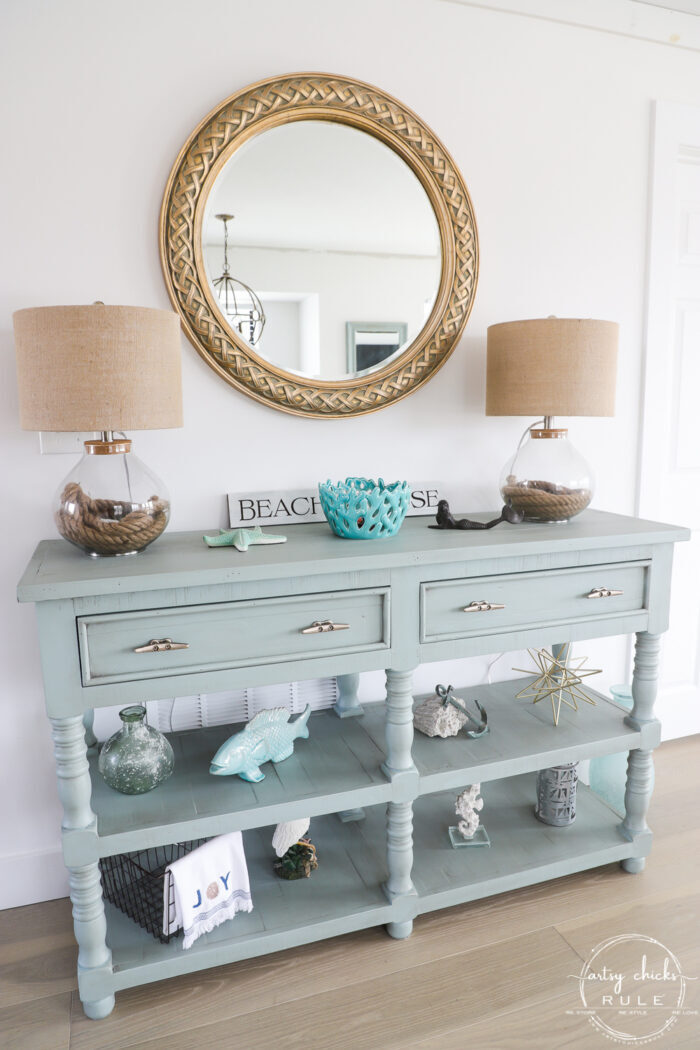 decorated aqua console with round gold mirror and two lamps