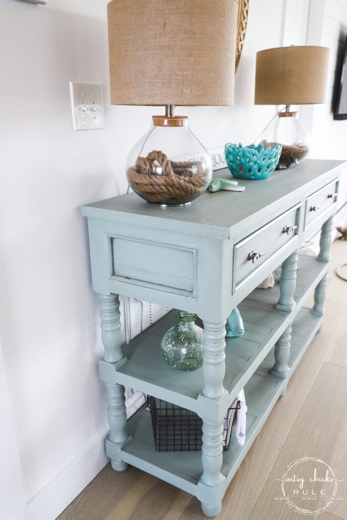 sideview of aqua console table with decor and lamps on wood floor