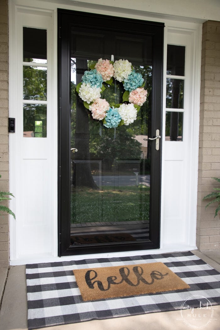 black front door, plaid rug, pink and teal wreath