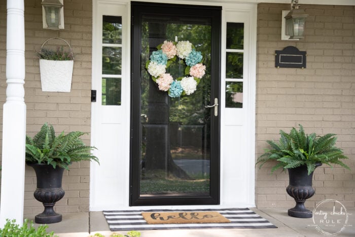 black front door with wreath and green ferns on each side