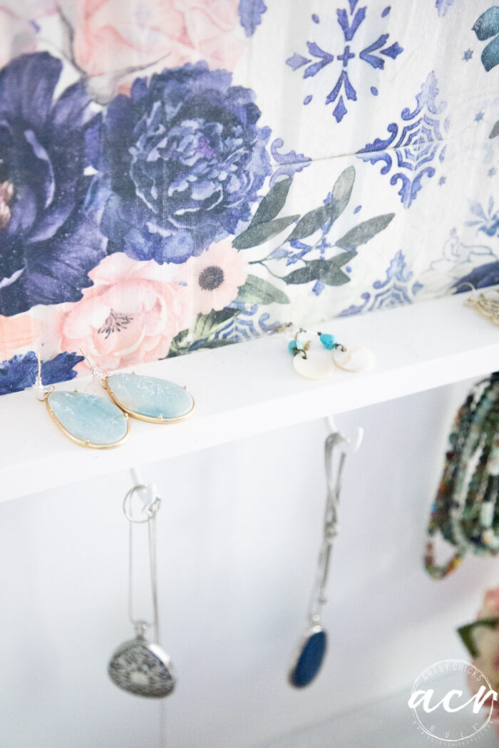 up close of blue floral shelf showing earrings on shelf and necklaces hanging