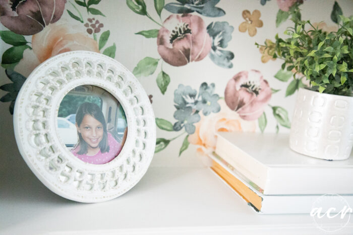 close up of white framed picture, white books and green plant