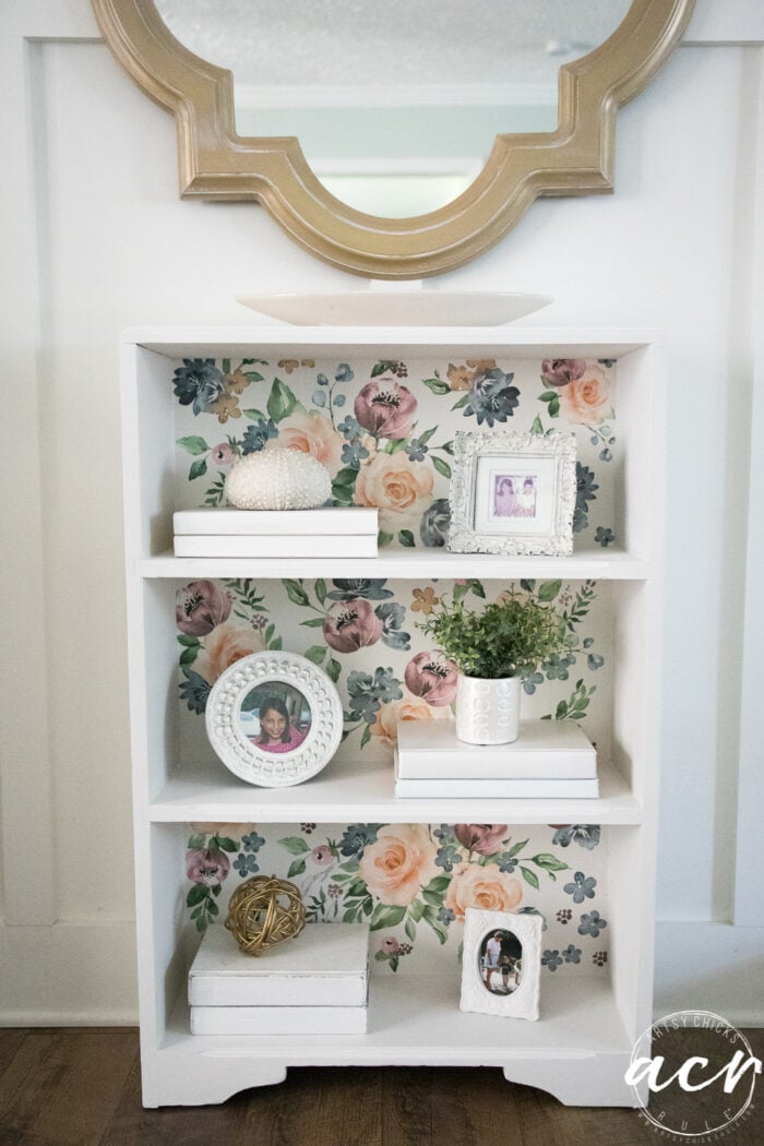 white bookcase styled with gold mirror over top