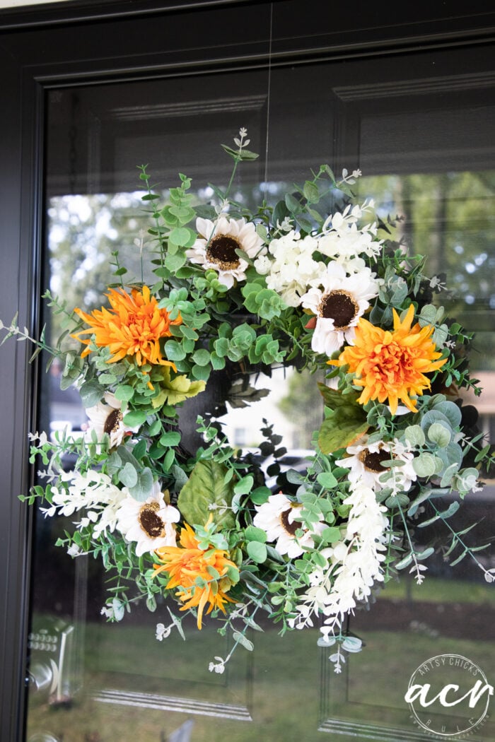 orange flowers white sunflowers on green wreath hanging on door