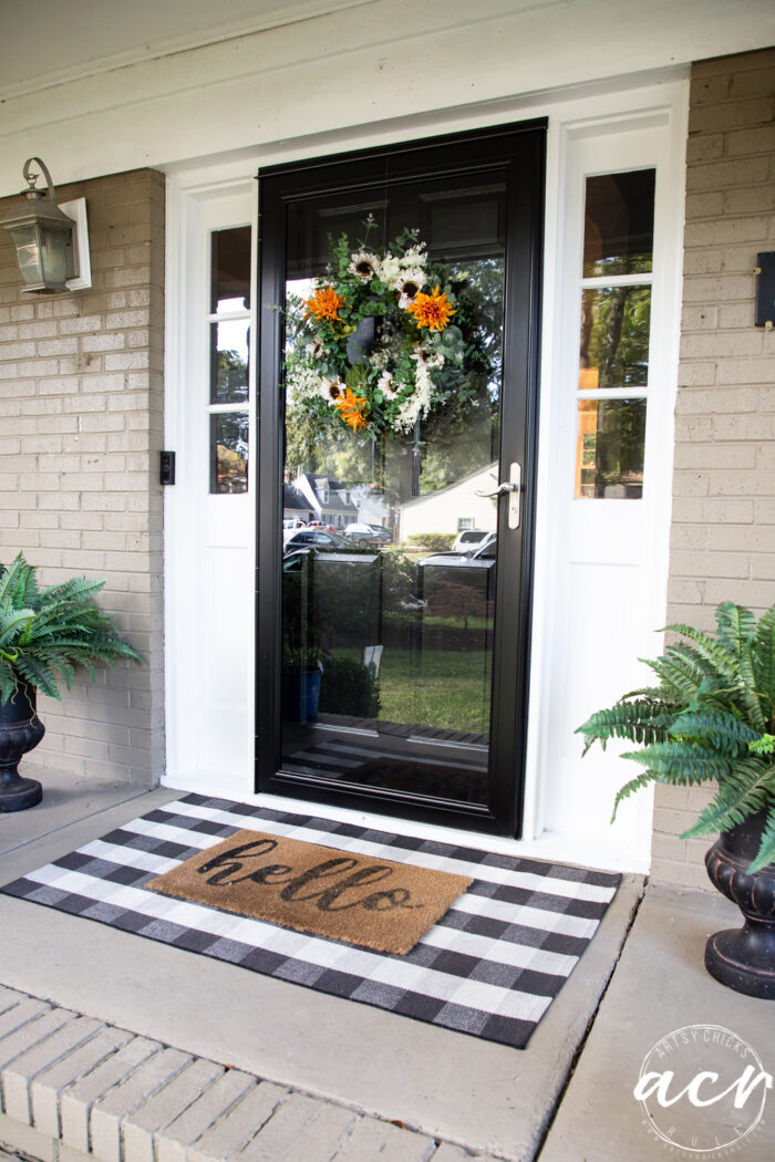 front porch with black door and fall wreath, green ferns