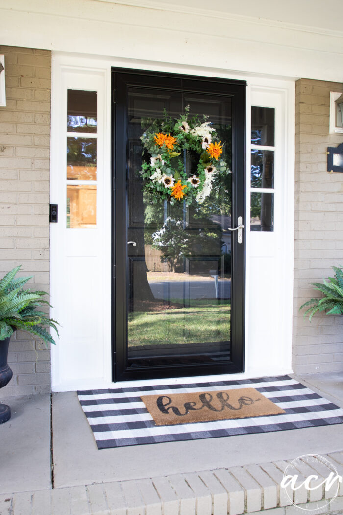 black front door with fall wreath and hello mat