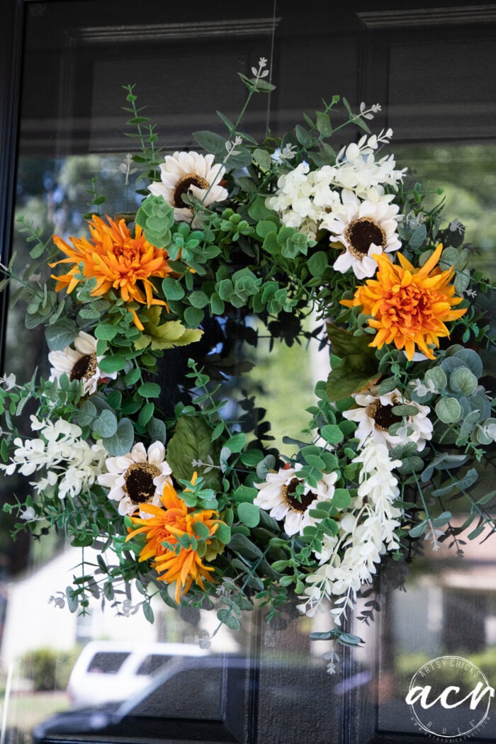 green wreath on door with orange flowers and white sunflowers