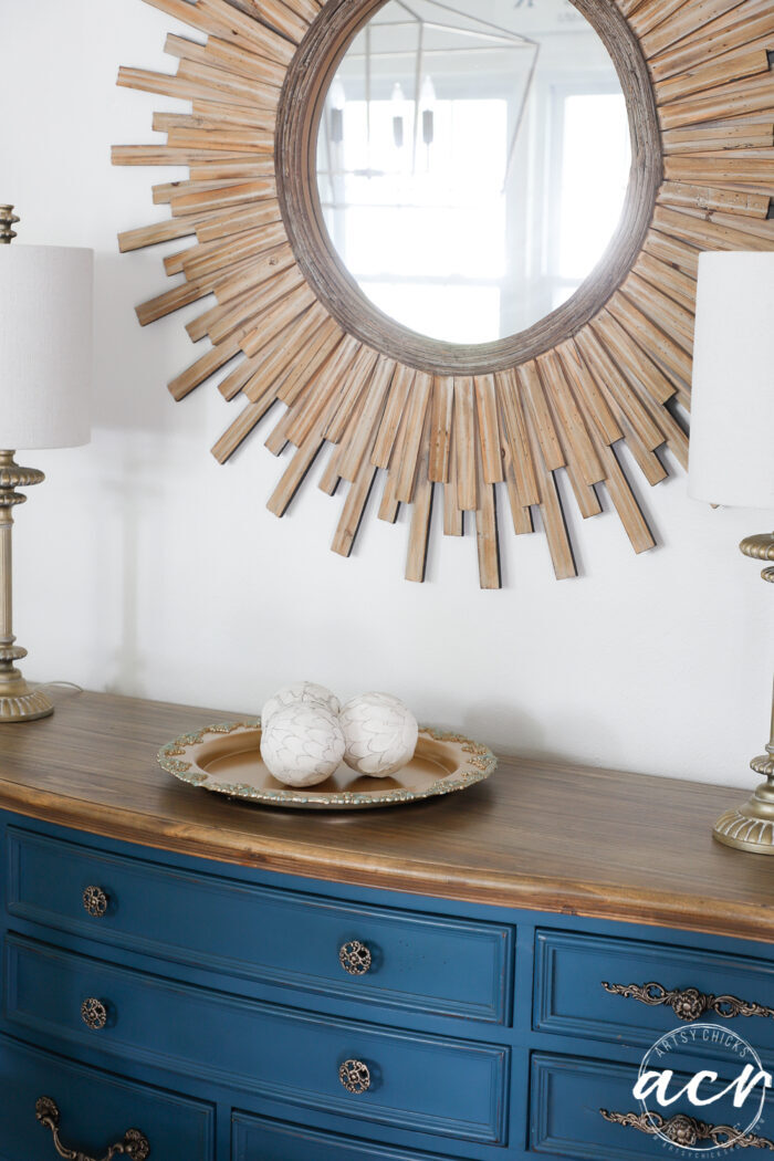 blue dresser with wood starburst mirror and gold tray