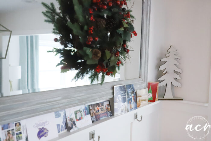 green and red wreath on mirror with Christmas cards on shelf below