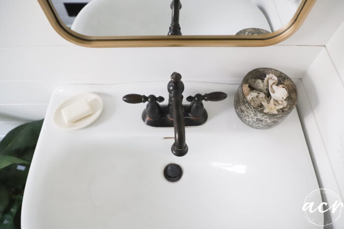 white sink with bronze faucet, soap and bowl of seashells