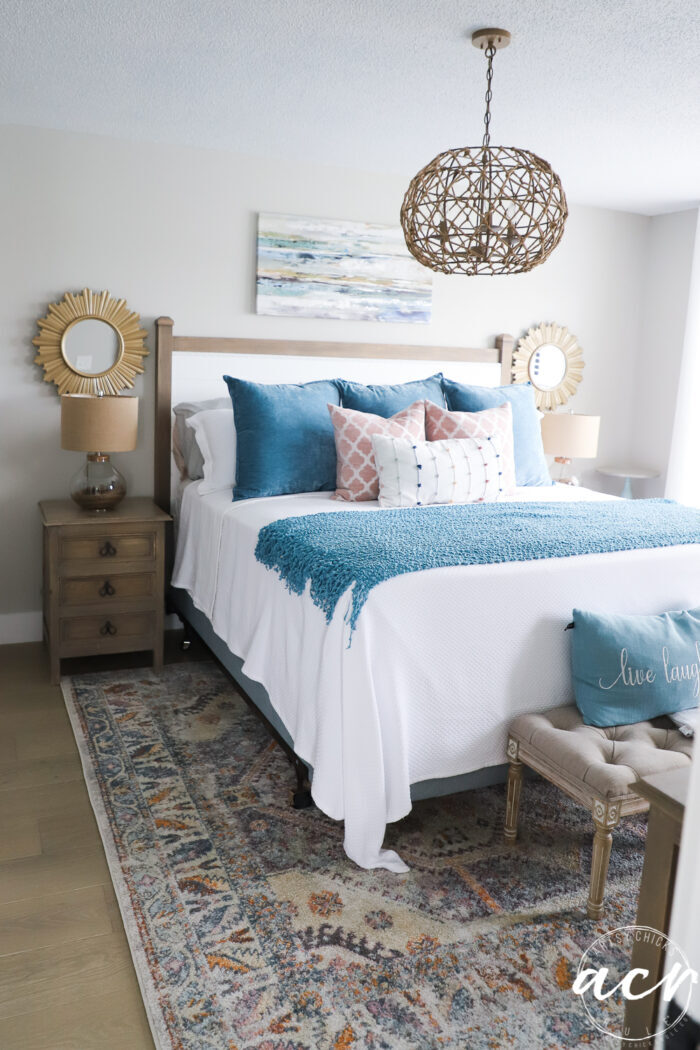 full bedroom shot with gold mirrors on wall, blue and white bedding, colorful rug and rope light fixture