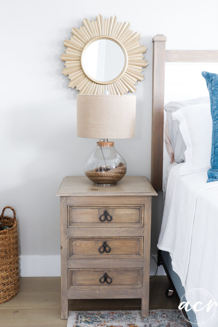 driftwood colored nightstand beside bed with lamp and gold mirror over top