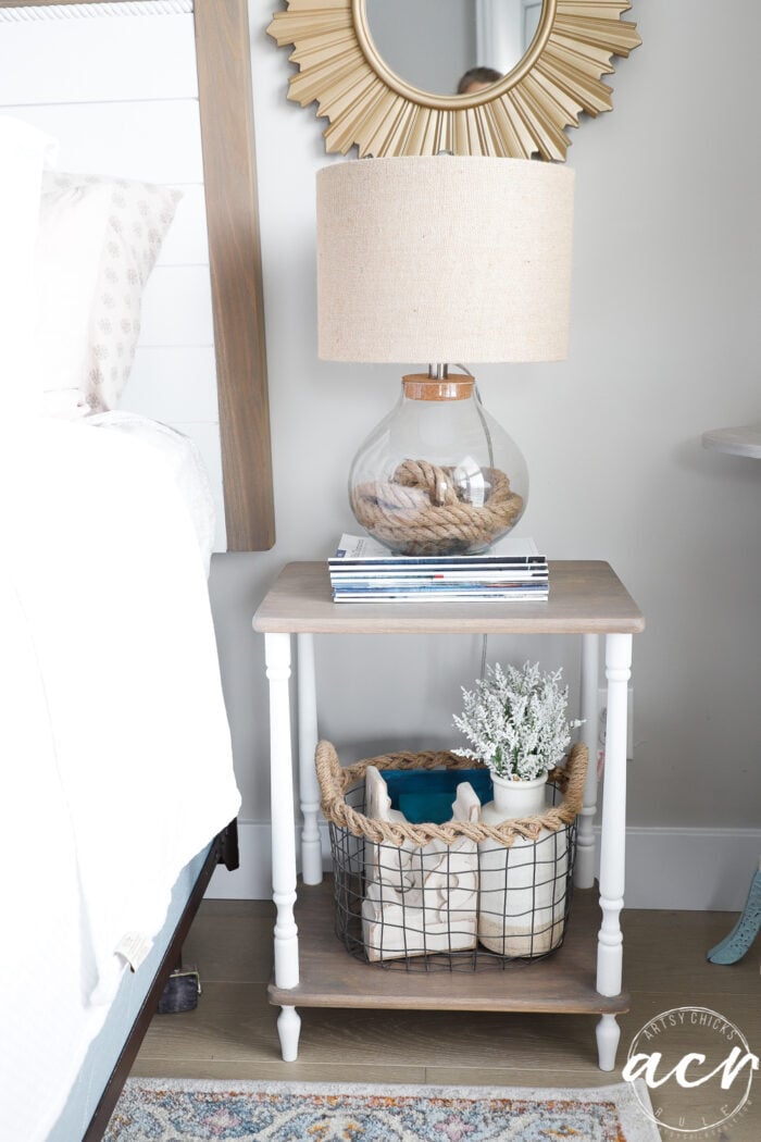 tan and white table with lamp and magazines, basket below with decor items