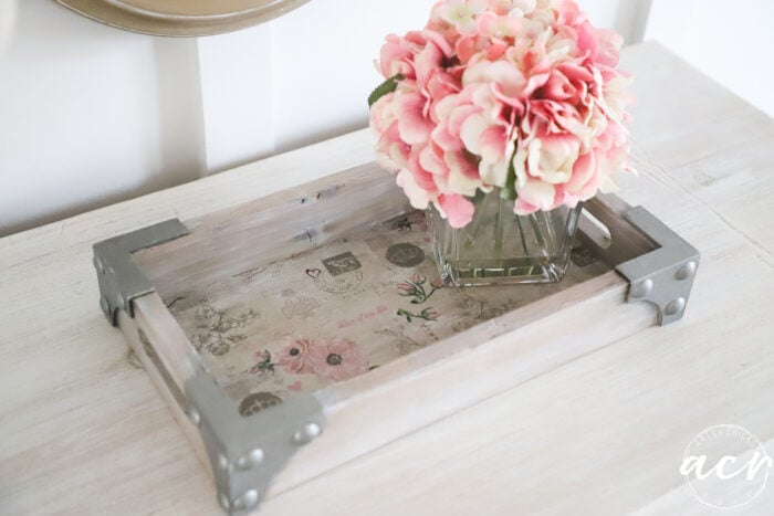 tan wood tray with metal corners and floral base