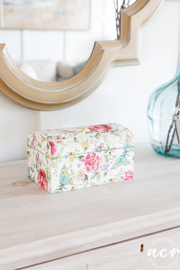 floral box on dresser with gold mirror on wall