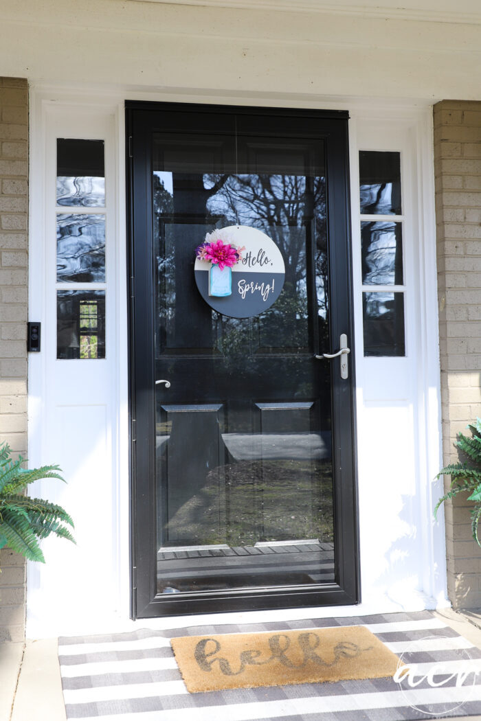 black and white round sign with hello spring, blue jar and pink colorful flowers, on glass front door