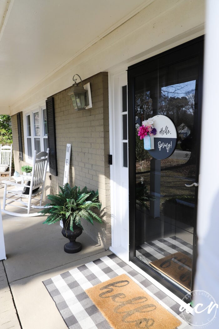 black and white round sign with hello spring, blue jar and pink colorful flowers, on glass front door with porch view