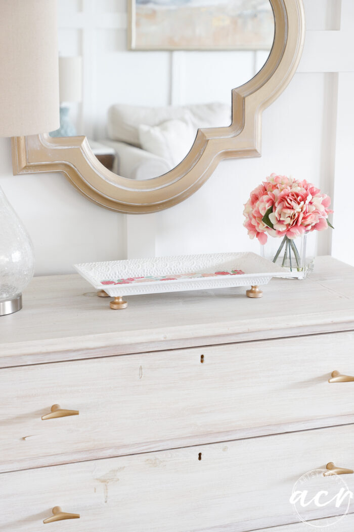 washed wood dresser with white floral tray and gold mirror on wall