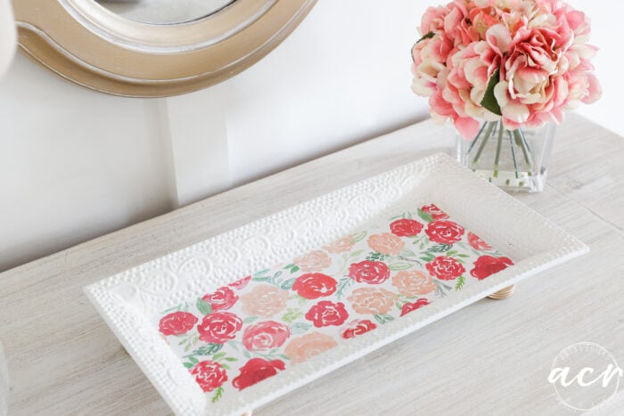 white tray with knob feet and pink flowered scrap paper on the bottom