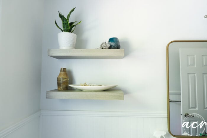 wood look shelves with decor and rounded gold mirror on wall
