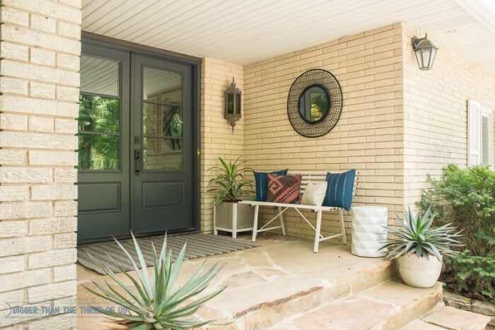 beige brick front porch with cactus plants and white bench