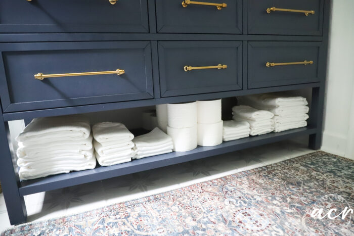 lower shelf of vanity with white towels and toilet paper