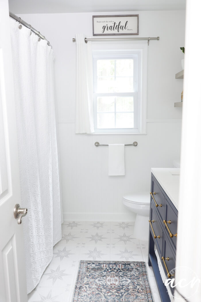 full bathroom shot with window, curtain, rug and blue vanity