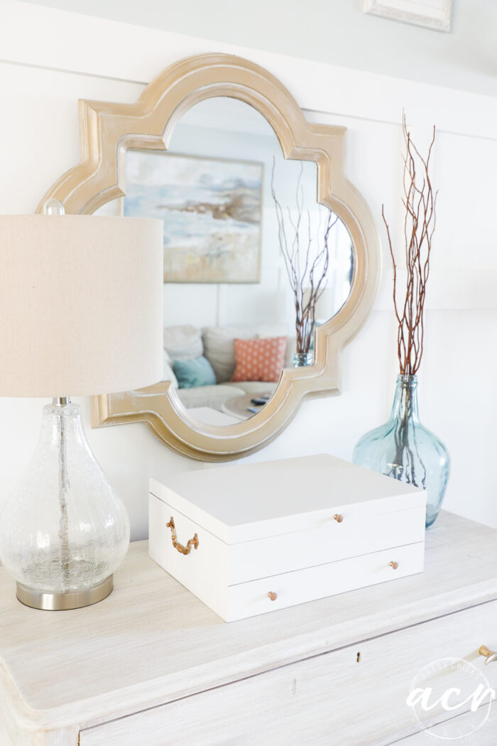 gold mirror on wall, white box on dresser