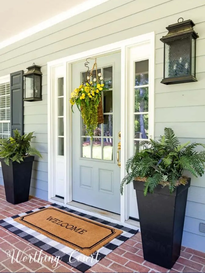 green house with welcome mat at front door and planters on each side