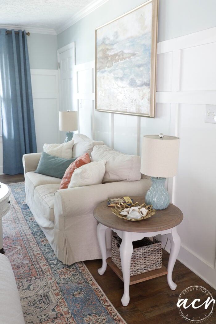 white room with dark floors, blue curtains, driftwood stained side table and tan couch