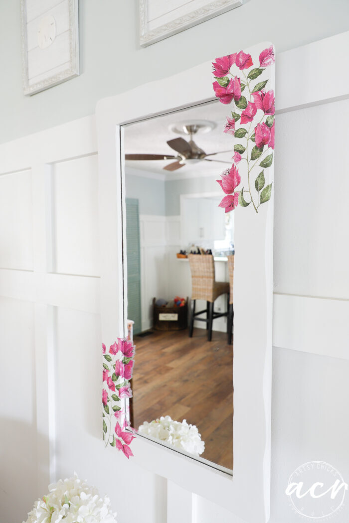 white framed mirror on wall with pink floral corners