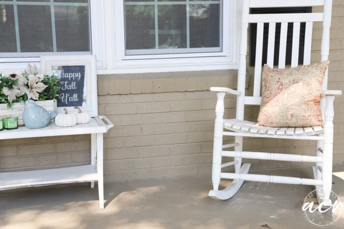 white rocker with rust colored pillow and white table with fall decor