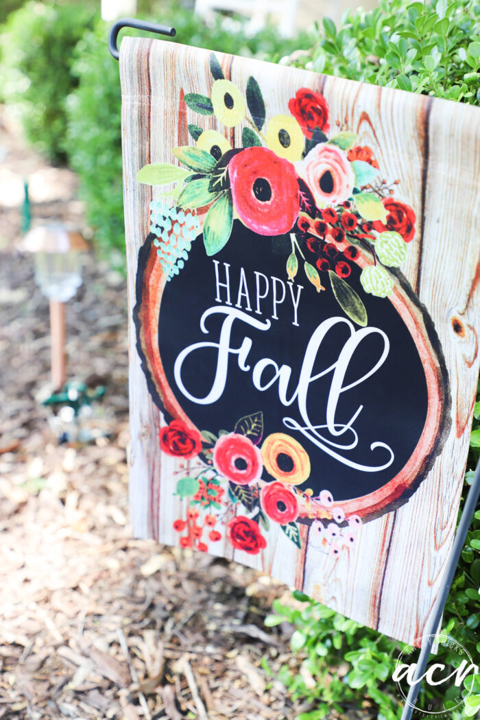 happy fall flag on hanger in flower bed