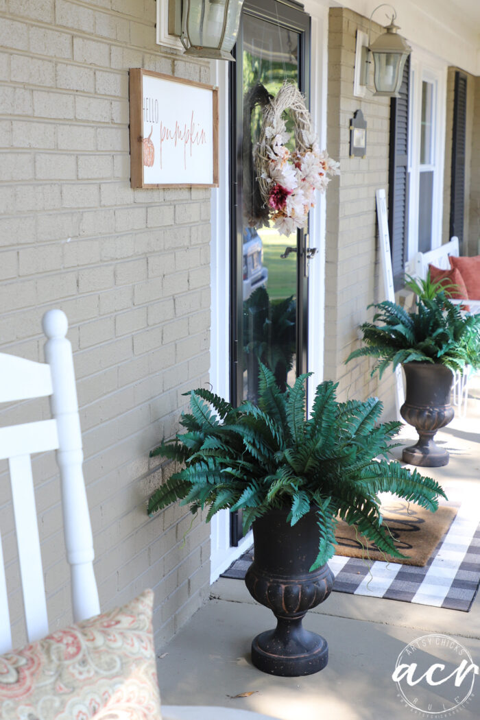 looking down porch with 2 green ferns rust colored pillows and white bench