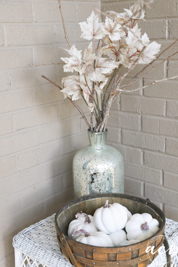 jar on white table with branches, white leaves and basket full of white pumpkins